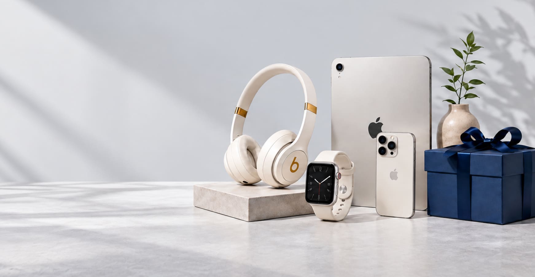 Headphones, watch, tablet, phone and a navy gift box on a light grey backdrop